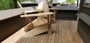 Two Adirondack chairs sitting on a wood Veranda. Side profile.